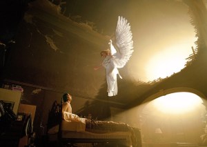 An angel appears, floating in the air above the bed of a man who is sitting up.